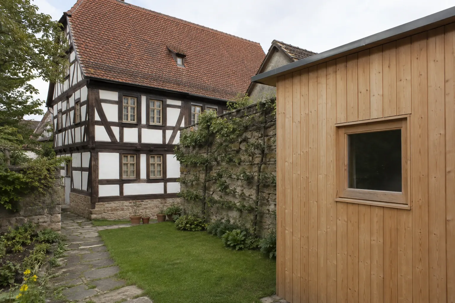 Kleines modernes Gartenhaus im Garten hinter einem denkmalgeschützten Fachwerkhaus